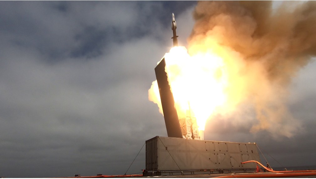 一枚 SM-6 飛彈拖著火焰與白色尾煙，從艦艉的貨櫃式發射器垂直升空